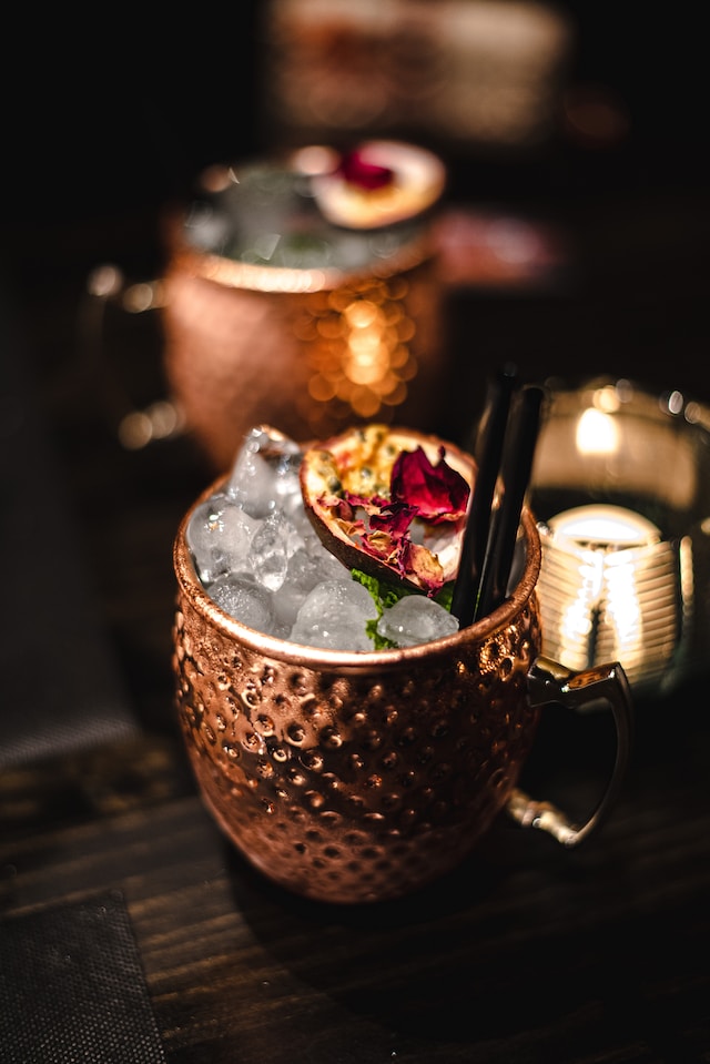 Cocktails in textured copper mule mugs, with ice and pomegranate garnish.